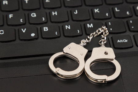 Cybercriminal concept. Keychain handcuffs on the black computer keyboard.の写真素材
