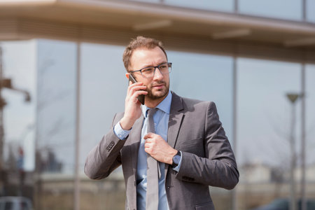 Young professional in suit having a call. He is walking outside the office and wearing suit 