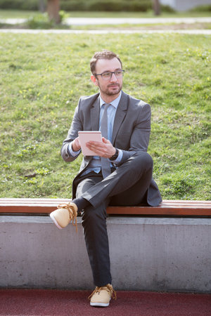 Young businessman using a tablet device on a bench in the parkの写真素材