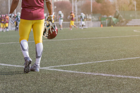 Player in red and yellow jersey holding sport helmet on the football fieldの写真素材
