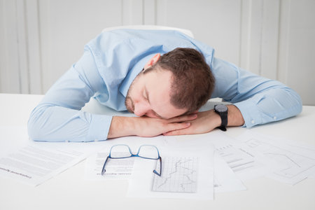 Businessman tired of overtime work. He is sleeping at the desk surrounded with different paper documents.の写真素材