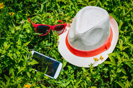 Straw hat, red sunglasses and white smartphone placed on the green grass. Spring is about to start. の写真素材