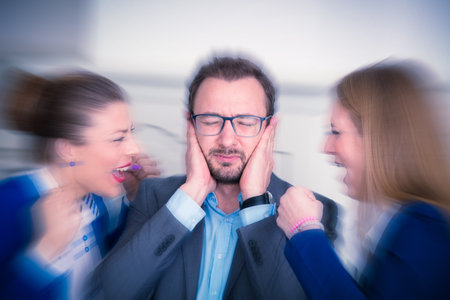 Businesspeople sitting at the office desk. Annoyed businessman covering his ears with hands and two...