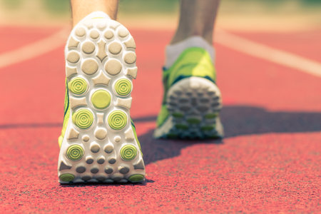 Back side view close up shot of feet with running shoes on the red running track. Jogging, training,...
