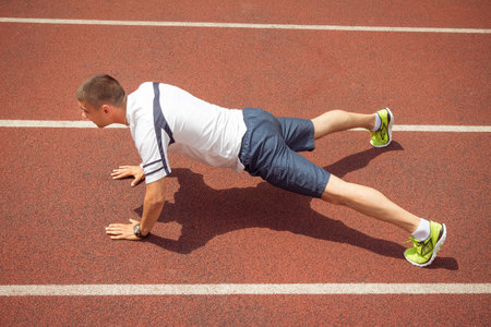 Side view of fitness man doing push-ups on running track outdoors. Male athlete exercising. Sport...