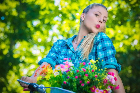 Portrait of pretty young female with pursed lips on bicycle with basket full of colorful flowers. Summer, nature, fashion and recreation concepts.  の写真素材