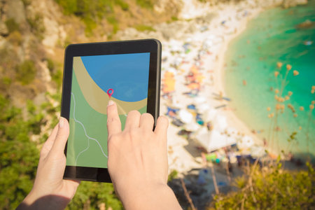 Female hands holding digital tablet device with gps navigation map application on the hill above the beautiful beach. Vacation and travel concepts.の写真素材