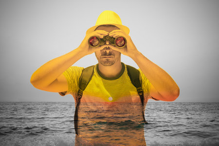 Young tourist guy looking at sunset over sea by using binoculars. Double exposure conceptual photo. Vacation concept.  の写真素材