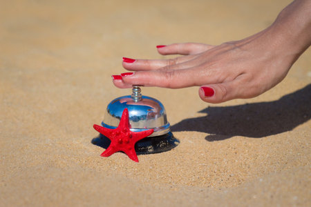 Close up of female hand pressing service bell on sandy beach. Summer vacation concept.の写真素材