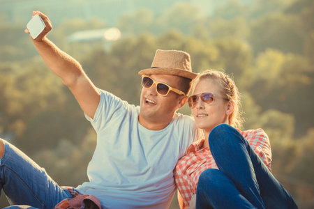 Young tourist couple in love taking selfie with smart phone above the city at sunset. Summer, travel, vacation and technology concepts.の写真素材