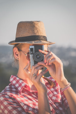 Portrait of young female taking photo with old retro camera outdoors.の写真素材