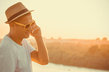 Trendy guy with hat talking on smart phone outdoors. Technology, summer and vacation concepts. Space for copy.の写真素材