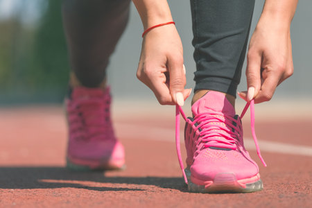Running shoes - closeup of woman tying shoe laces. Female sport fitness runner getting ready for jogging outdoors on running track.の写真素材