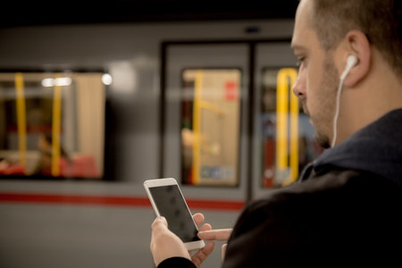 Urban man using smartphone and earphones at the train stationの写真素材