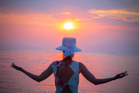 Female with spread hands looking at sunset on the beach. Summer season concept.の写真素材