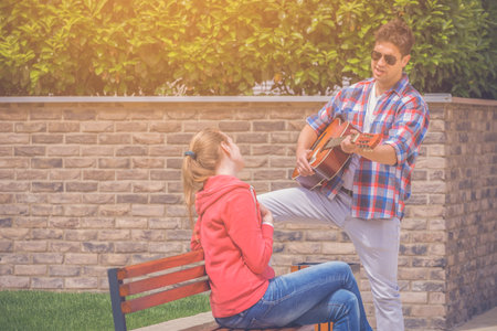 Romantic man singing song and playing guitar to his girlfriend in the parkの写真素材