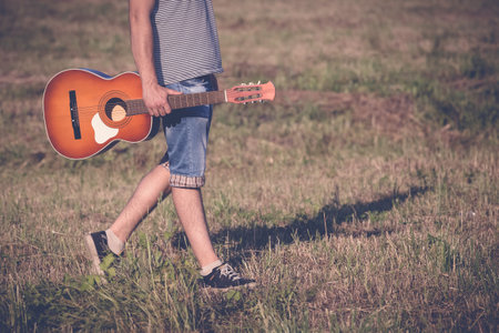 Fashionable guy with acoustic guitar walking in natureの写真素材