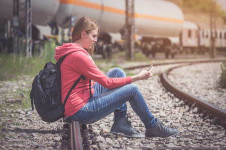 Traveler sitting on rail way and looking at mobile phoneの写真素材