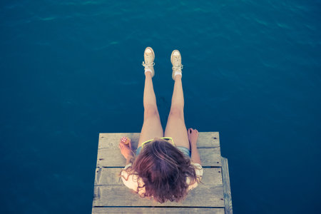 Top down viewpoint of young modern female sitting on pier. Summertime concept.の写真素材