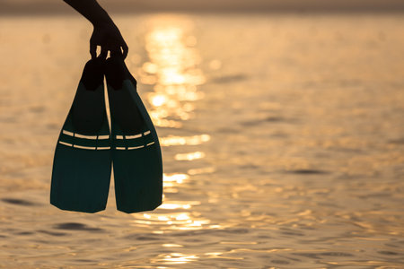 Man holding snorkel fins on beach at sunsetの写真素材