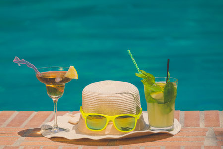 Female sunhat, sunglasses and cocktails at the poolside. Summertime concept. の写真素材