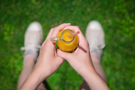High angle view of female holding glass bottle of fresh orange juice with drinking straw and standing on field. Healthy lifestyle concept.の写真素材