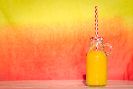 Glass bottle of orange juice with drinking straw on table. Space for copy. Healthy eating concept. の写真素材