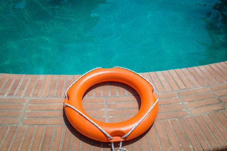 Orange lifebuoy or ring buoy on edge of swimming pool outdoorsの写真素材
