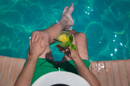 High angle view of tourist holding glass of mojito cocktail at the poolsideの写真素材