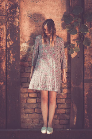 Young trendy fashionable hipster woman in dress on old brick wall backgroundの写真素材