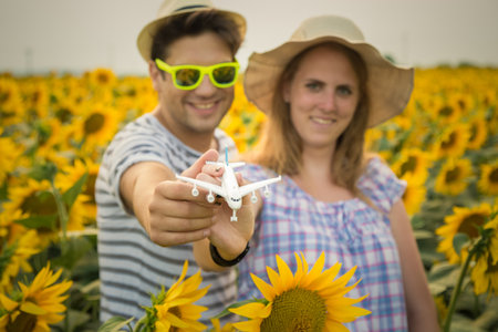 Portrait of young couple holding airplane model toy in sunflower field. Love, summer vacation and travel concepts.の写真素材