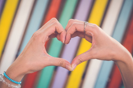 Close up of female hands making heart shape with her hands against background in different colors の写真素材
