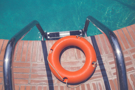 Orange lifebuoy or ring buoy on edge of swimming pool next to staircaseの写真素材