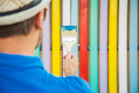 Rear view close up of modern man holding paint brush against colorful wooden fenceの写真素材