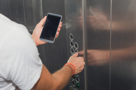 Close up of young modern man holding blank screen smart phone in elevator and pressing floor button