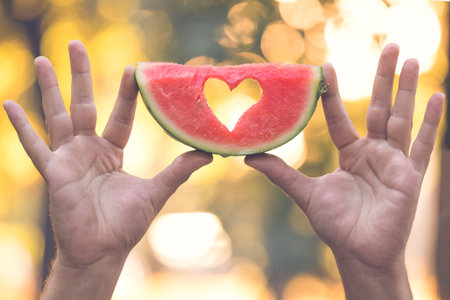 Close up of man hands holding watermelon slice with heart shape in natureの写真素材