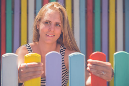 Portrait of beautiful trendy, fashionable woman standing between colorful fence and wooden wall. Fashion and beauty concepts.の写真素材