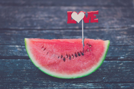 Close up of watermelon slice with love sign on table in the park. Healthy eating and summertime concepts.の写真素材