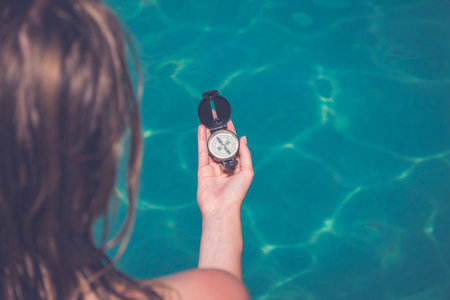 High angle view of female tourist holding compass against blue swimming pool water surface. Summer vacation and travel conceptsの写真素材