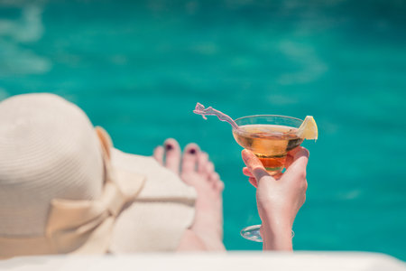 Rear view of female lying in sunbed and holding glass of copacabana cocktail at the poolsideの写真素材