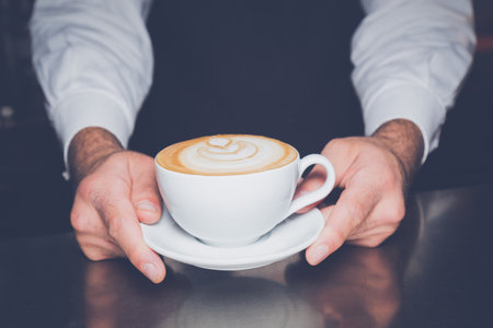 Close up of barista holding a cup of fresh and hot latte macchiato coffee の写真素材