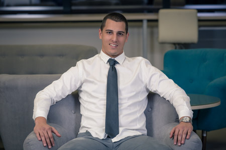 Handsome confident executive smiling and sitting in office lobbyの写真素材