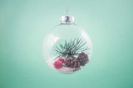 Close up of transparent Christmas decoration ornament with pine branch, pine cone, red berries and snowの写真素材