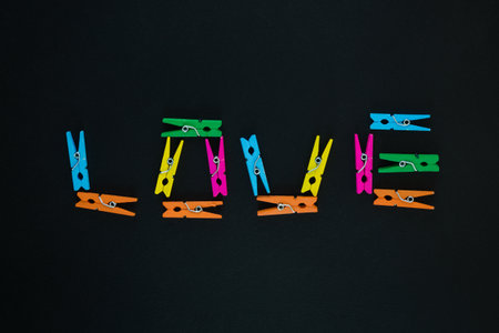 Love text made of colorful wooden clothes pegs on black background
