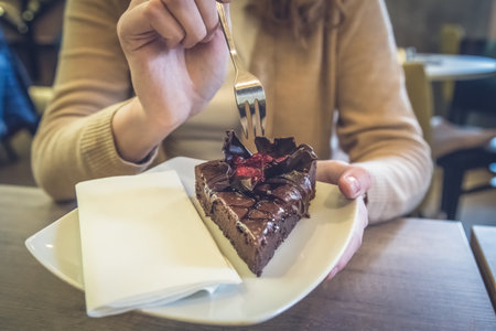 Female hand holding a fork and plate with piece of homemade chocolate cake in restaurantの写真素材