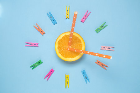 Flat lay of orange fruit half with two drinking straws in form of clock hands and clothespins arranged in circle. Time for healthy drink minimal concept.の写真素材