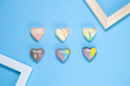 Flat lay of colorful praline heart shape chocolate and frames against pastel blue background....