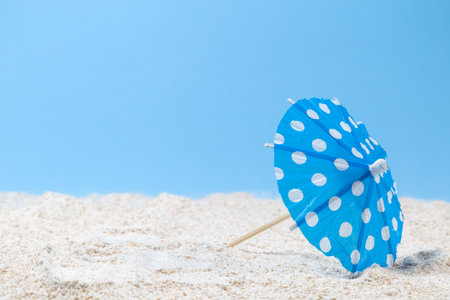 Cocktail umbrella on sandy beach against blue sky background minimal concept. Space for copy.の写真素材