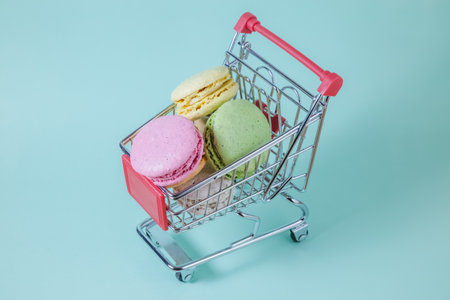 Studio photo of macarons in small metal shopping cart on green background. Minimal concept.の写真素材