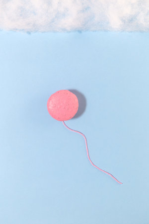 Pink macaron and rope in form of balloon on blue paper sky background with clouds made of cotton wool. Minimal conceptの写真素材